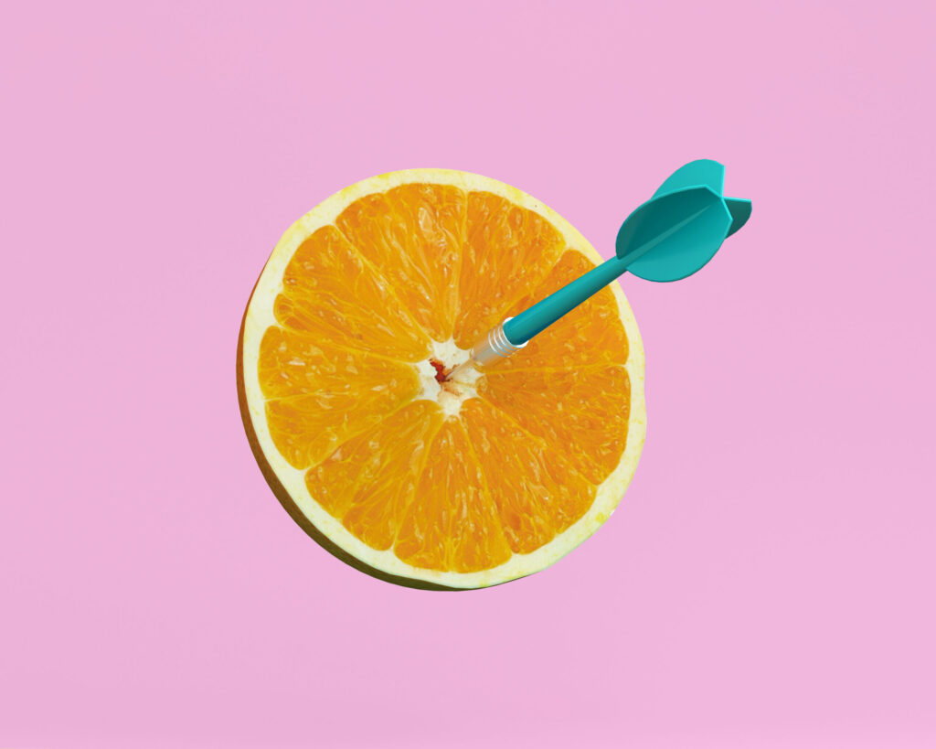 An orange slice with a blue arrow embedded in the center on a pink background